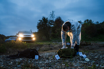 Forensic police investigator collecting evidence at the crime scene in nature at night murder...