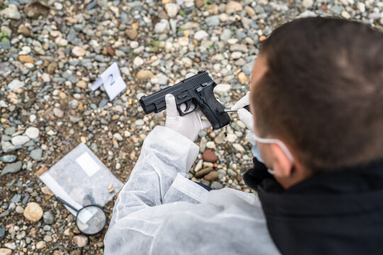 top view back of the police detective forensic investigator on the crime scene hold gun evidence on the beach or sand rocks used for murder or shooting with tag during investigation copy space