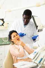 Asian woman talking with african-american man dentist about toothache during visit in dental clinic.