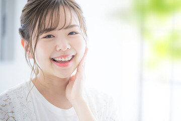 Fototapeta premium 笑顔のカメラ目線女性のアップ 緑の前ボケあ 右にコピースペースあり