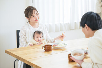 Obraz na płótnie Canvas 食卓で赤ちゃんと一緒にご飯を食べるママさんとあやすパパさん