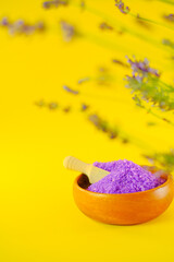 Obraz na płótnie Canvas lavender salt.purple sea bath salt in a round wooden cup and lavender on a bright yellow background.body cosmetic with lavender extract.Aromatherapy and spa.lilac salt with lavender extract
