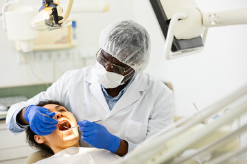 Focused african american stomatologist treating teeth to female patient in modern dental office..