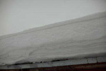 Snow on roof. Snowy winter. Layer of ice accumulated on wall.