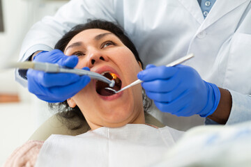 African american dentist is treating female patient which is sitting in dental chair