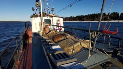 A ship carrying cargo. Clip. Ships sailing in a spring melting river with a large cargo against the background of forests with snow around and blue sky above.