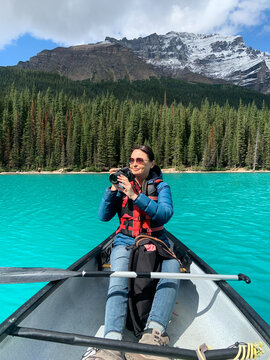Woman in canoe in middle of Moraine Lake taking pictures with digital camera