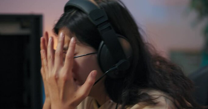 The face of woman wearing glasses and headset upset about losing computer game broken gamer waving hands covers face screaming, crying, panicking sadness from defeat in virtual esports