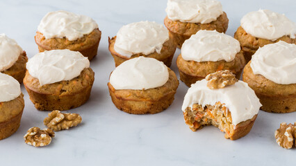 Several carrot cake muffins topped with cream cheese frosting, ready for eating.