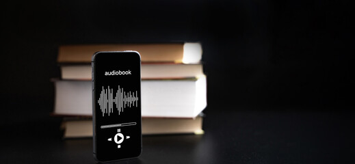 Audio book education. Phone screen with audio book app on paper books black background. Online learning, home school concept.