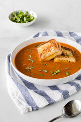 A bowl of tomato soup with small grilled cheese sandwich squares on top.