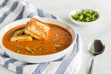 A bowl of tomato soup with small grilled cheese sandwiches on top.