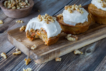 Fototapeta na wymiar Carrot cake muffins with cream cheese icing and walnuts on a small wooden board.