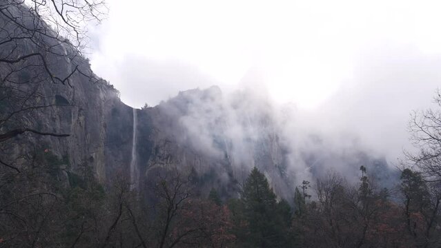 Foggy mountain, bare cliffs, steep rocks, misty calm autumn weather, Yosemite valley waterfall, California, USA wilderness. Scenic crags, bluffs and silent fall forest. Brume or haze clouds timelapse.