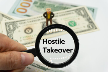 Hostile Takeover.Magnifying glass showing the words.Background of banknotes and coins.basic concepts of finance.Business theme.Financial terms.