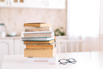 Stack of books with glasses standing on a table in front of the kitchen.