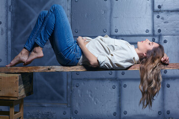 Portrait of young beautiful blonde woman is sitting on a board on metal wall background.