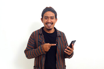 Happy asian man in javanese traditional costume standing while pointing at his phone. - obrazy, fototapety, plakaty
