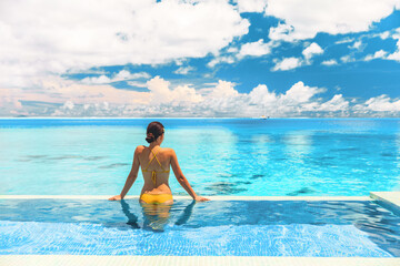 Travel vacation luxury resort idyllic overwater bungalow villa woman relaxing by infinity pool. Elegant beautiful lady in yellow bikini, by perfect blue ocean water - obrazy, fototapety, plakaty