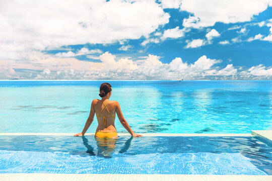 Travel vacation luxury resort idyllic overwater bungalow villa woman relaxing by infinity pool. Elegant beautiful lady in yellow bikini, by perfect blue ocean water
