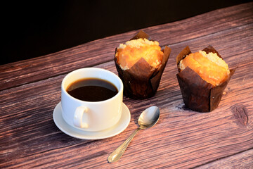 Two fresh cupcakes and a cup of hot black coffee on a wooden table.