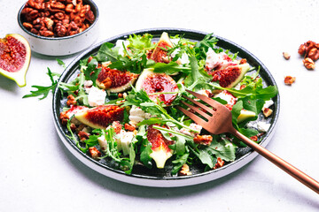 Delicious summer salad with sweet  figs, white feta cheese, walnuts, arugula and jam vinegar dressing on white table background, top view, negative space