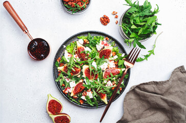 Delicious summer salad with sweet  figs, white feta cheese, walnuts, arugula and jam vinegar dressing on white table background, top view, negative space