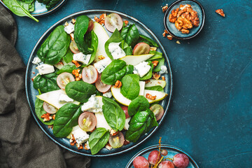 Delicious summer salad with pear, grapes, roquefort cheese, spinach, walnuts on blue table background, top view, negative space