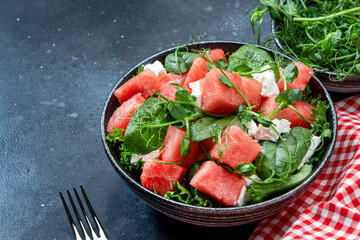 Delicious summer watermelon salad bowl with feta cheese, spinach and pea sprouts on gray table background, top view, negative space