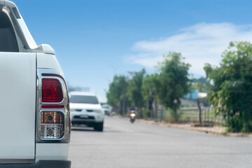 Rear side of white pick up car driving on the asphalt road in the city. with trees beside of the road and other cars. Under clear sky.