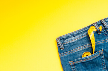measuring tape is in the back pocket of blue jeans on a yellow background, copy space. The concept...