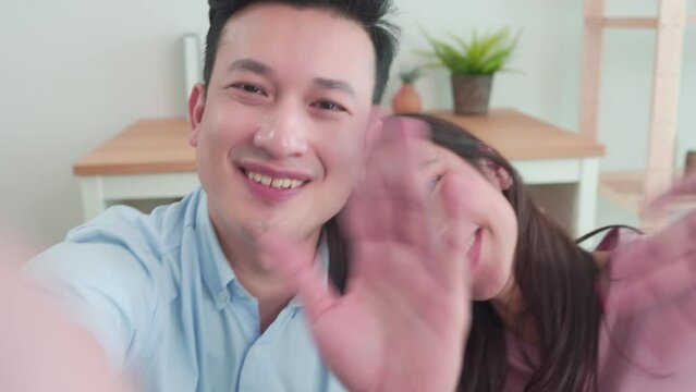 Family Young asian couples using smartphones to take selfies on indoors home vacation. Husband hugging wife with love while posing having fun, cheerful on video call with happy smile at living room.