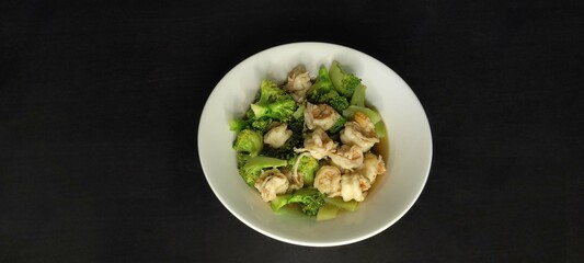 Stir fried broccoli with shrimp in white plate on black background from top view
