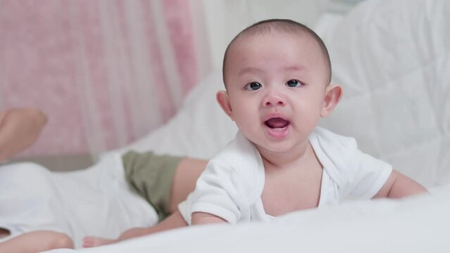 Cute Asian newborn baby boy lying play on white bed with smile happy face. While your mother takes care nearby. Little innocent new infant adorable child in first day of life. Mother's Day concept.