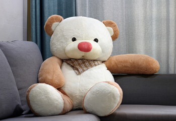 Big toy bear doll sitting and relaxing alone on big sofa.