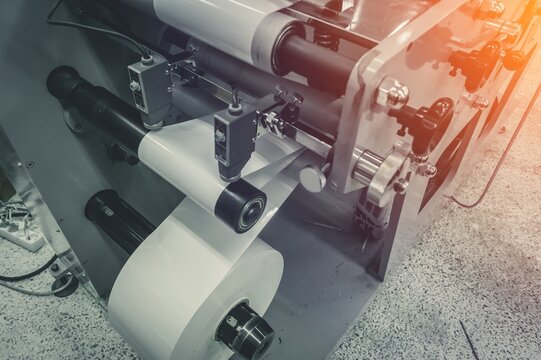 Roller of white printing paper for self-adhesive label on the shaft of the die-cutting machine in the printing house. Selective focus