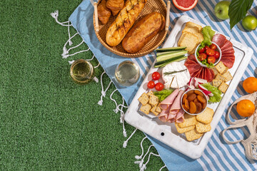 Picnic blanket with charcuterie boards, healthy food and wine in park on the grass on sunny day.