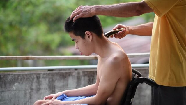 Young man with a disability on wheelchair giving dad a haircut, He had a tremor caused by Cerebral palsy has symptoms similar to Parkinson's disease,Health care for people with disabilities concept.