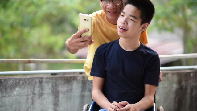 Young man with a disability and parent help to using mobile phone for selfie or social media, He had a tremor caused by Cerebral palsy, or CP, Ataxia has symptoms similar to Parkinson's disease.