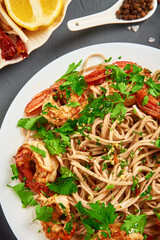 Stir fry noodle with shrimps, lemon and fresh parsley on white plate, soba with prawns, asian cuisine, top view