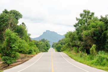 Fototapeta na wymiar An empty highway undulating road among the green trees and the huge mountains in front at Lampang, Thailand