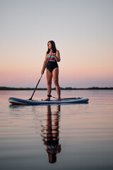 Portrait of calm relaxed middle aged woman sup boarding with oar in hands looking away on lake with...
