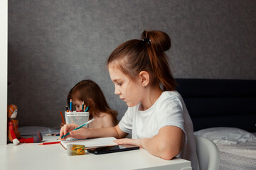 Preteen girl sitting at table, holding mobile phone, drawing, learning. Kid's actiivities at home.