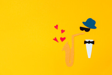 International Jazz Day. Silhouette of a musician with a saxophone, which hearts and flew out on a yellow background, cutted out of felt. Copy space. Flat lay