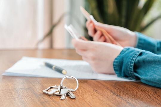 Close up of key with keychain lies on the table. Defocused person's hands counting money at the background. Concept of leasing and mortgage