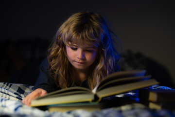 Child reading a book in bed before going to sleep. Little boy lying on bed reading book at home....