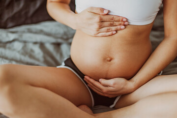 Fototapeta na wymiar Pregnancy belly stretch marks and linea nigra. Pregnant woman caressing holding stomach during first trimester. Skincare body care health concept