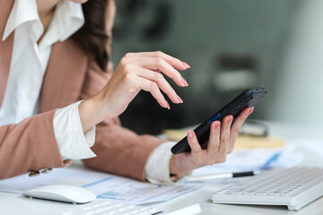 Close-up of female business person hands using smart phone while working on computer at modern office