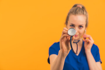 Fototapeta premium let's listen to your lungs - blonde nurse with stethoscope medium closeup studio shot orange background medical concept . High quality photo