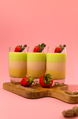 Fresh creamy dessert in glass made of kiwi, vanilla and mango with strawberry and chocolate on wooden tray.